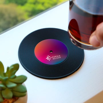 Someone setting a drink down on a branded vinyl coaster outside.