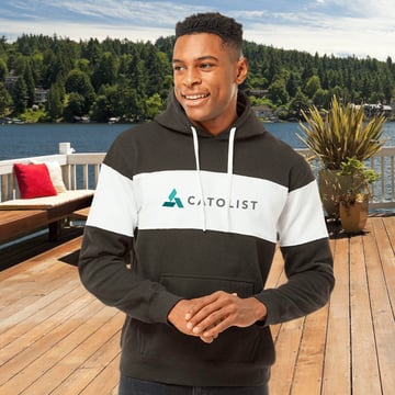 A man wearing a branded retro hoodie outside near a lake.