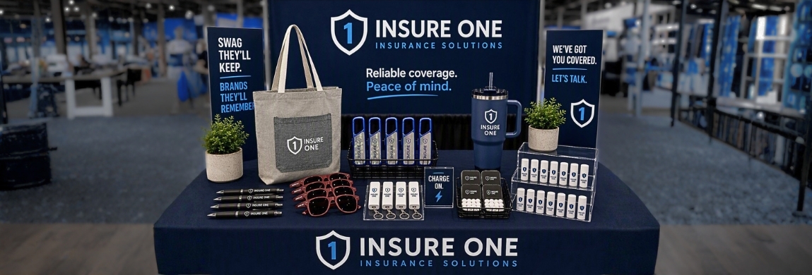 Trade show booth displaying branded promotional products including a canvas tote bag, tumbler, sunglasses, pens, power banks, lip balm, and mint tins on a navy tablecloth.